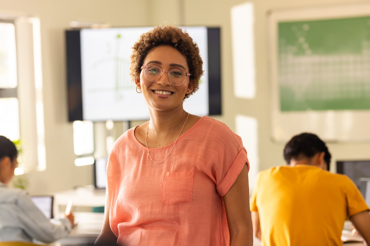Smiling teacher in classroom with students working on laptops in high school. Education, technology, teaching, digital learning, teamwork, interactive